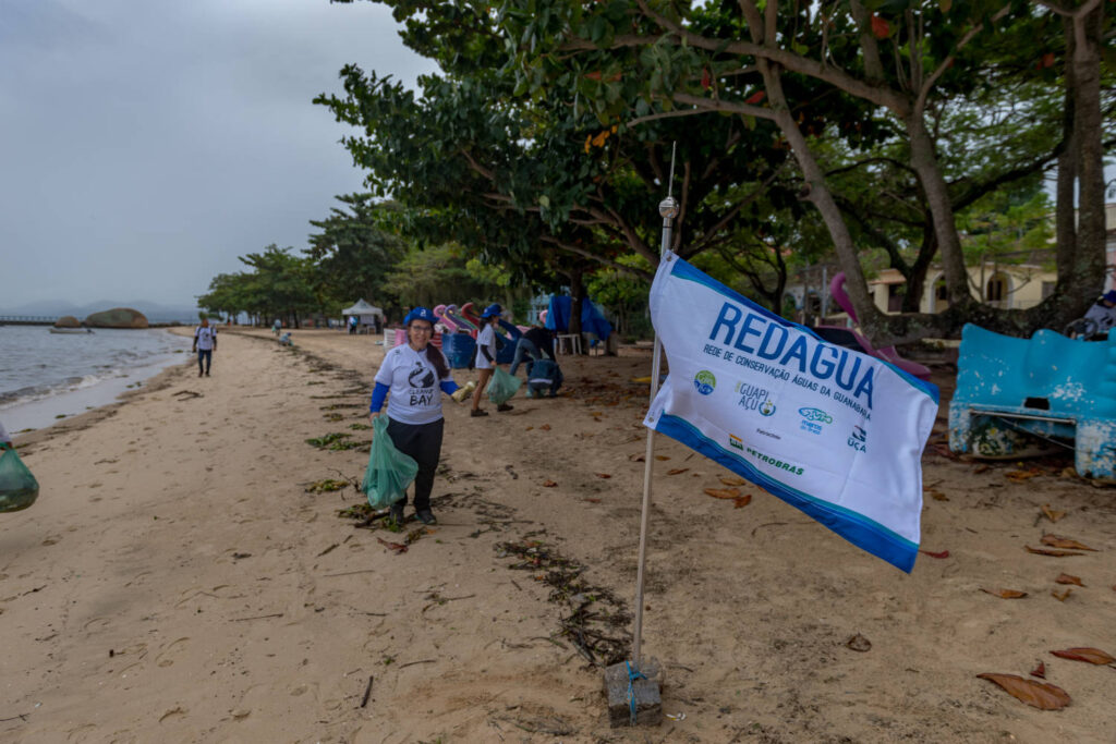 Grupo de pessoas realizam retirada de lixo em orla de praia.
