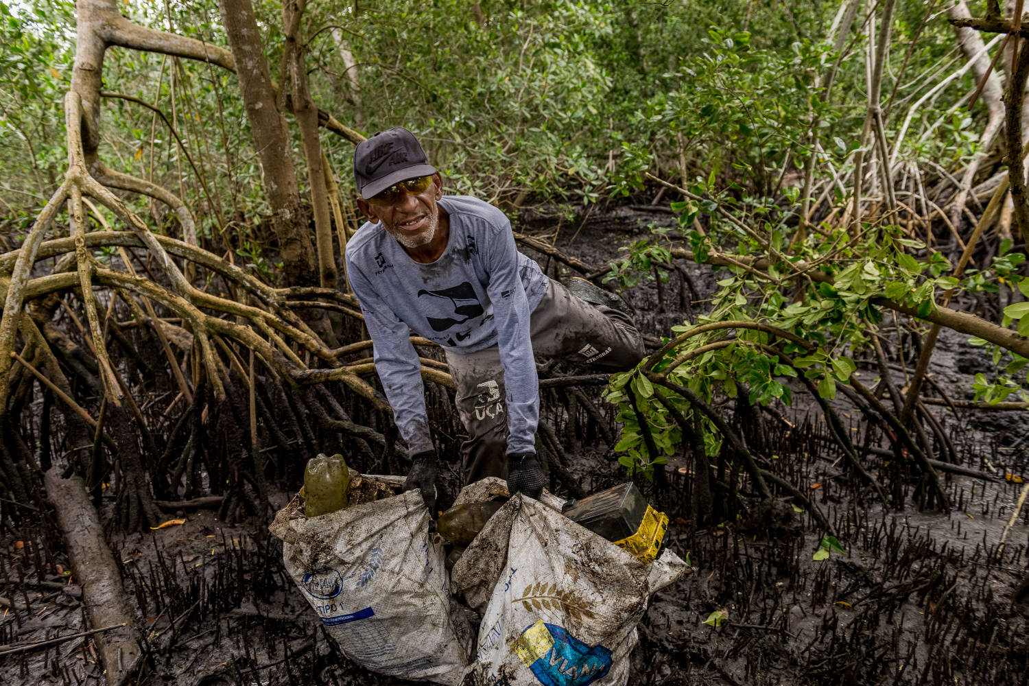 Homem recolhe lixo em área de mangue