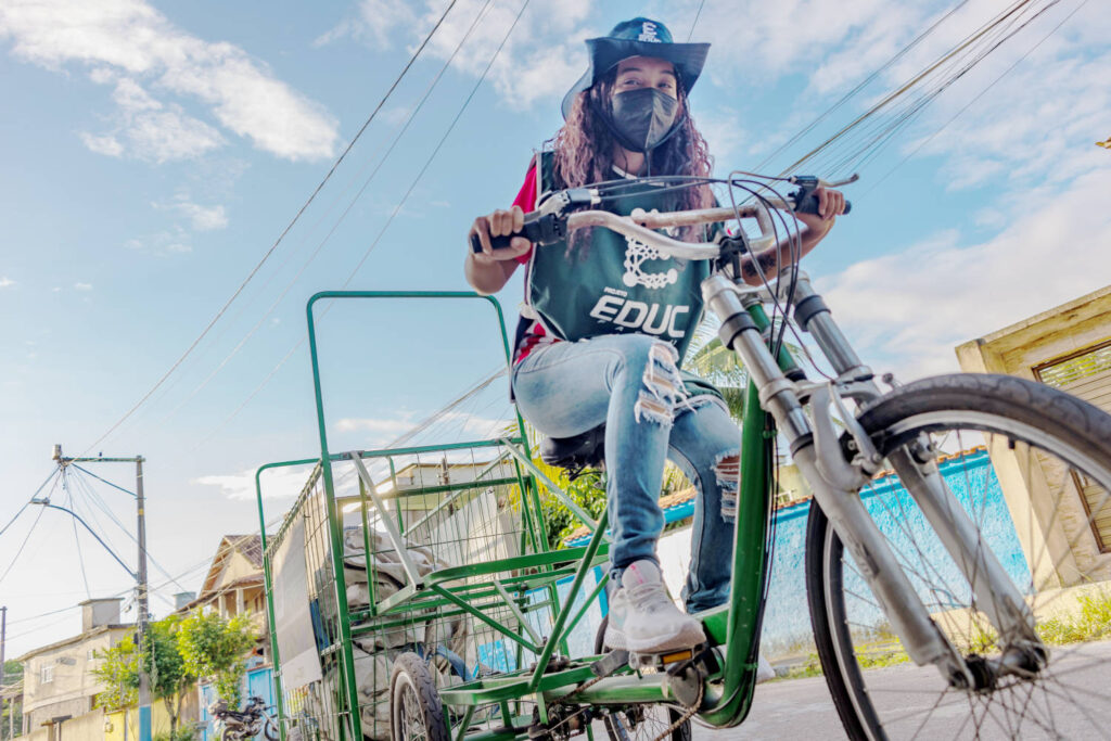 Jovem mulher pedala bicicleta para coletar materiais recivláveis
