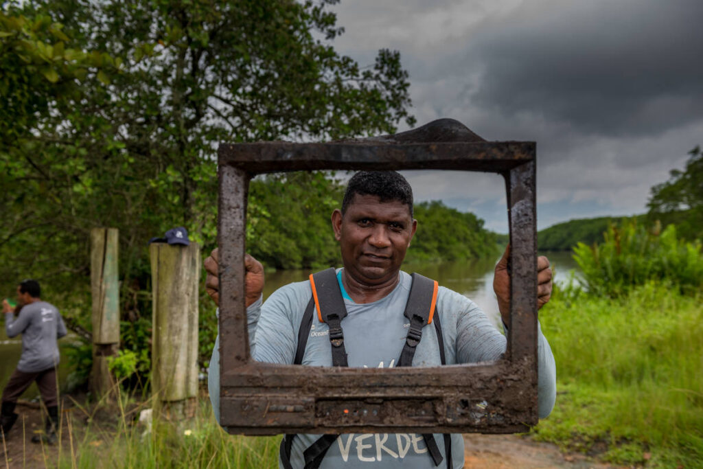 Homem exibe carcaça de antigo aparelho de tv encontrada em mangue